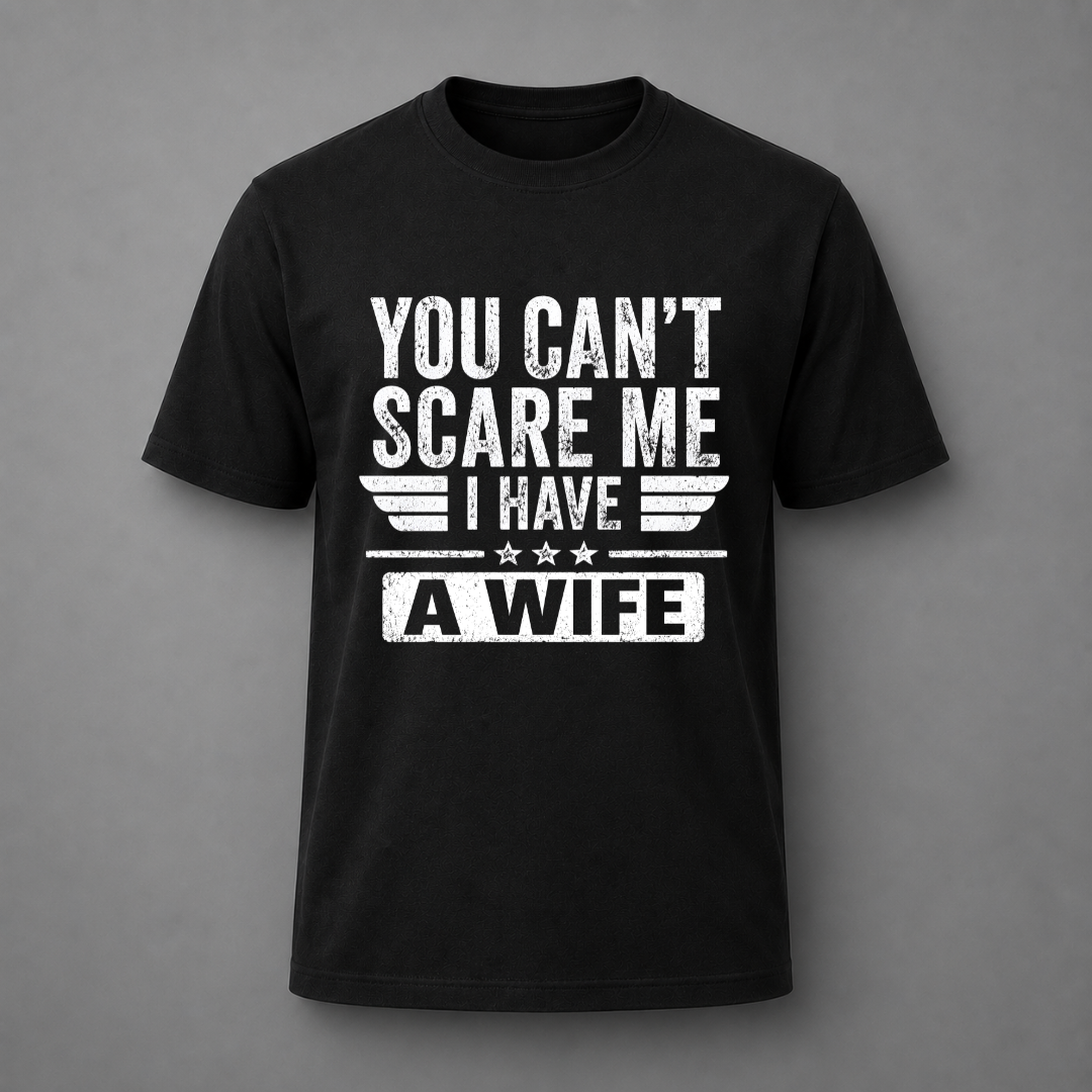 A black short-sleeve crewneck t-shirt with a distressed white graphic print on the front that reads 'YOU CAN'T SCARE ME I HAVE A WIFE' with wing and star details, displayed against a solid gray background.