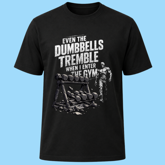 A black short-sleeve crewneck t-shirt with a humorous gym graphic. The graphic features the text 'EVEN THE DUMBBELLS TREMBLE WHEN I ENTER THE GYM' in distressed white lettering above an illustration of a weight rack and a muscular man, all set against a solid light blue background.