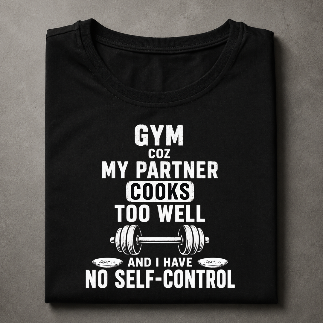 A black short-sleeve t-shirt with a humorous white graphic print that reads 'GYM COZ MY PARTNER COOKS TOO WELL AND I HAVE NO SELF-CONTROL' accompanied by a barbell illustration, displayed flat on a textured gray background.
