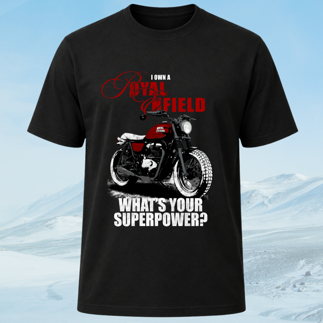 A black short-sleeve graphic t-shirt featuring a red and white motorcycle with the text 'I OWN A ROYAL ENFIELD' and 'WHAT'S YOUR SUPERPOWER?' in white and red lettering, set against a snowy mountain background.