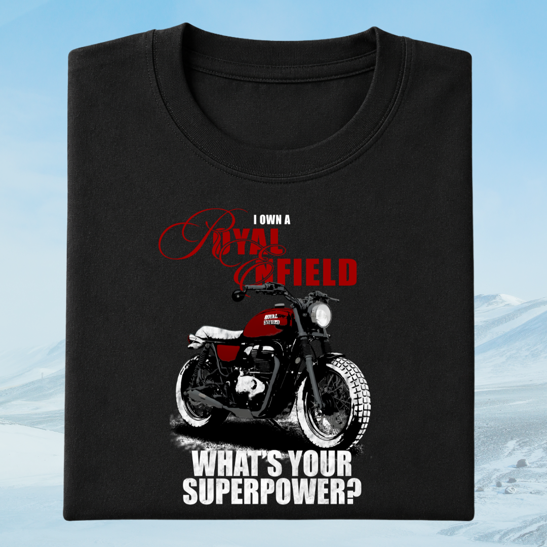 A black short-sleeve t-shirt with a graphic print of a red and black motorcycle, accompanied by the text 'I OWN A ROYAL BIKING FIELD WHAT'S YOUR SUPERPOWER?' in red and white, displayed against a snowy mountain background.