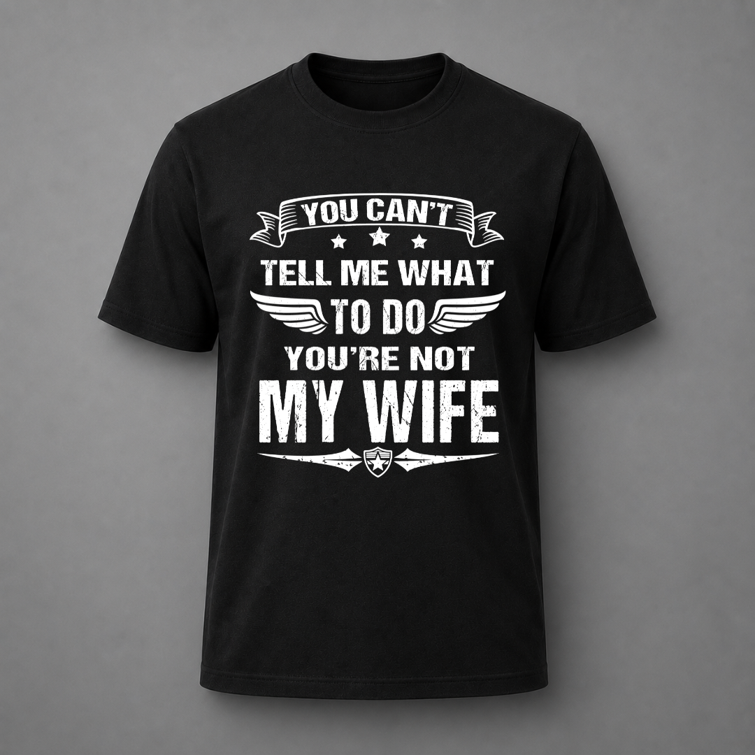A black short-sleeve crewneck t-shirt with a white distressed graphic text that reads 'YOU CAN'T TELL ME WHAT TO DO YOU'RE NOT MY WIFE' with wings and stars, displayed on a neutral gray background.