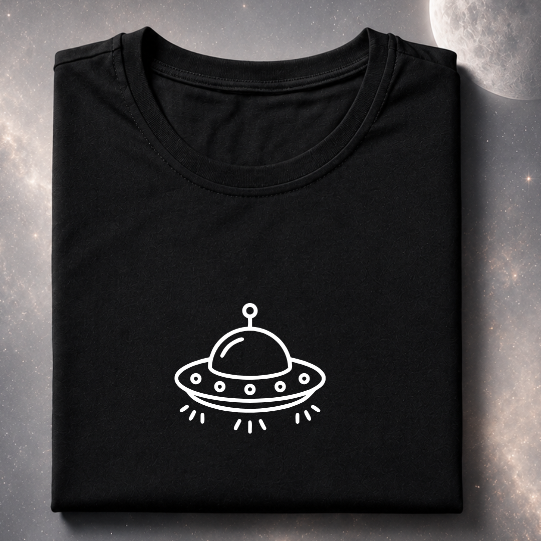 A folded black t-shirt with a white line art graphic of a UFO on the front, displayed against a dark, starry space background.