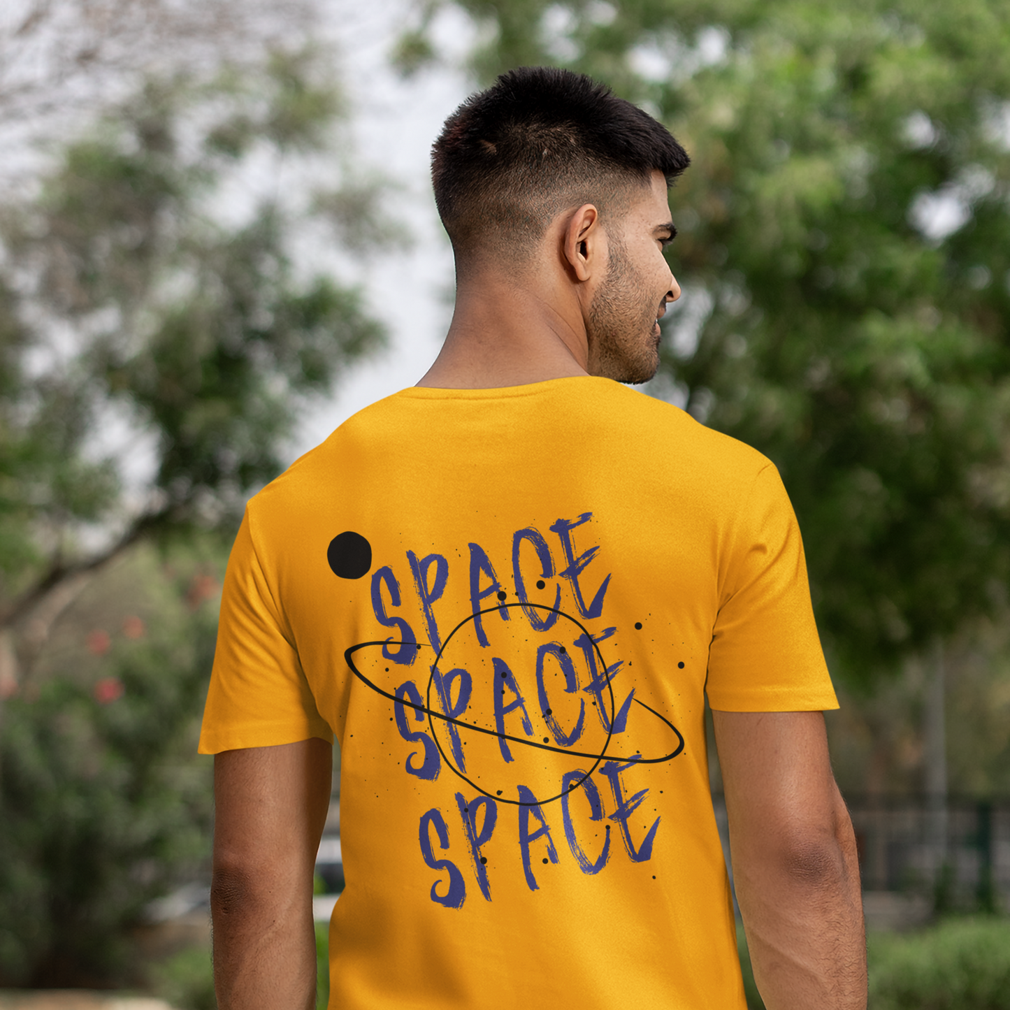 Man wearing a yellow t-shirt with 'SPACE' text, standing outdoors with greenery in the background.